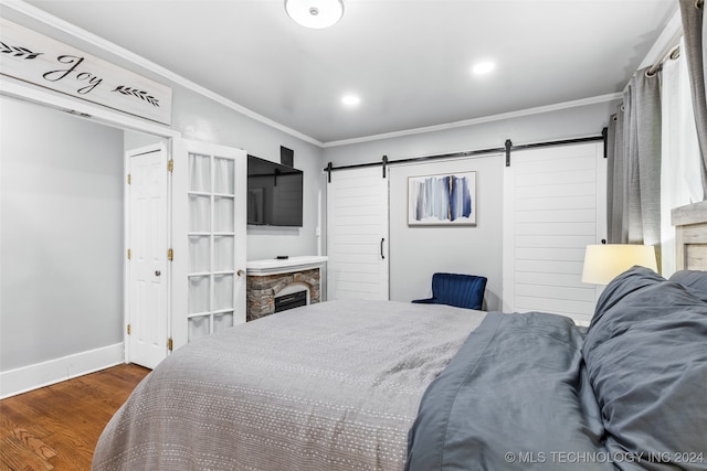 bedroom featuring a barn door, dark hardwood / wood-style flooring, crown molding, and a stone fireplace