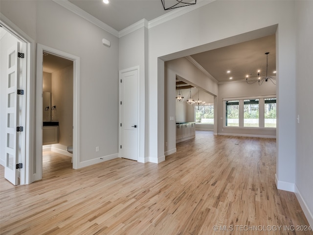 unfurnished living room featuring crown molding, light wood-type flooring, and an inviting chandelier