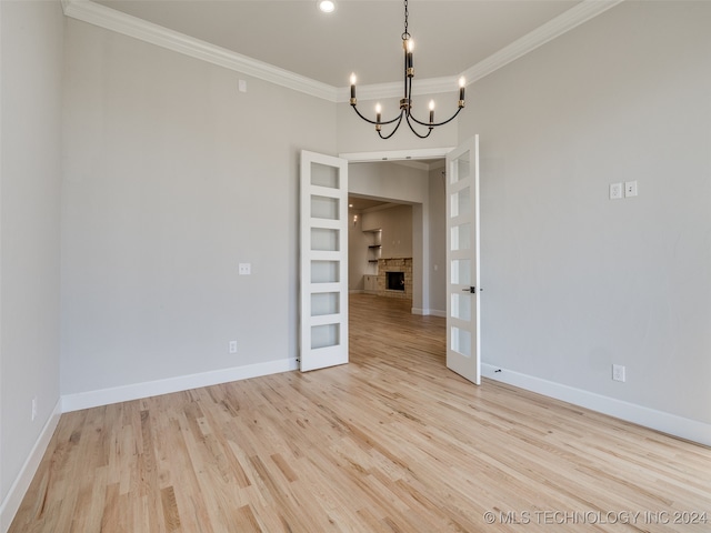 empty room with a chandelier, a stone fireplace, ornamental molding, and light hardwood / wood-style flooring