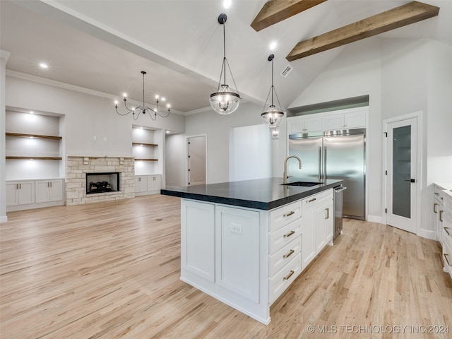 kitchen featuring a kitchen island with sink, white cabinets, a stone fireplace, sink, and beam ceiling