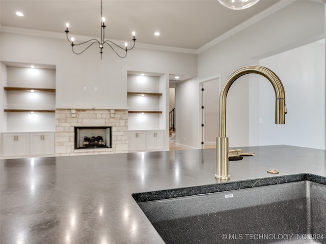 kitchen with a stone fireplace, built in features, crown molding, and sink