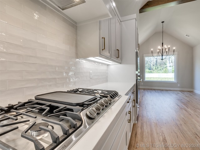 kitchen featuring stainless steel gas stovetop, lofted ceiling, white cabinets, light hardwood / wood-style flooring, and decorative backsplash