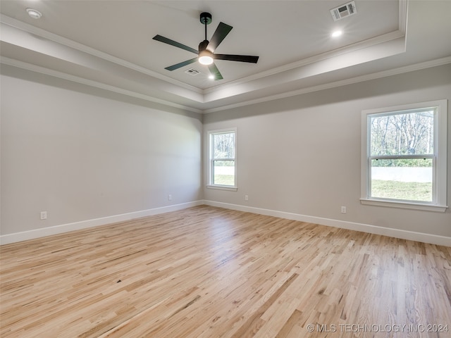 empty room with a healthy amount of sunlight, a raised ceiling, ornamental molding, and light hardwood / wood-style flooring