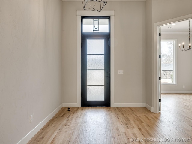 foyer entrance featuring crown molding, light wood-type flooring, and an inviting chandelier