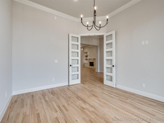 spare room featuring crown molding, an inviting chandelier, light hardwood / wood-style flooring, and french doors