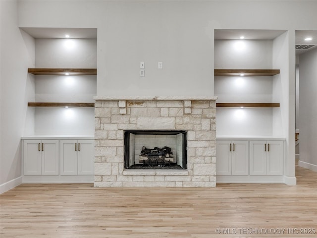 unfurnished living room with a stone fireplace, light hardwood / wood-style floors, and built in shelves