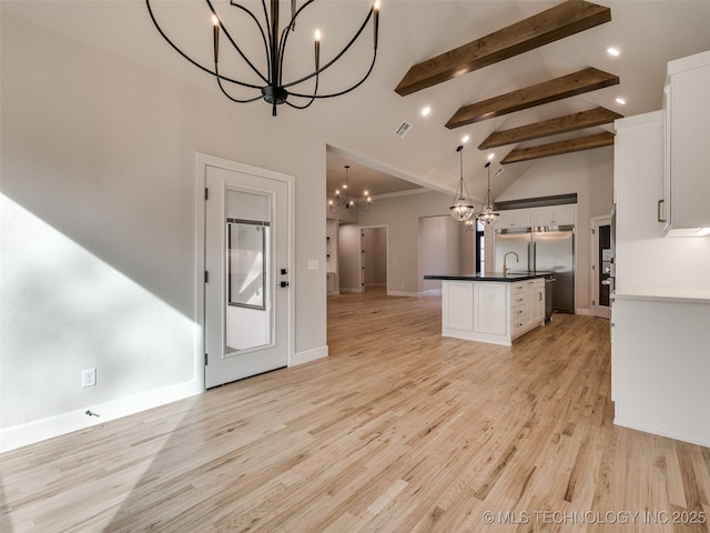 kitchen featuring stainless steel built in refrigerator, decorative light fixtures, a center island with sink, and white cabinets