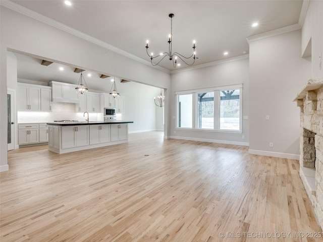 unfurnished living room with sink, crown molding, light wood-type flooring, a notable chandelier, and a fireplace