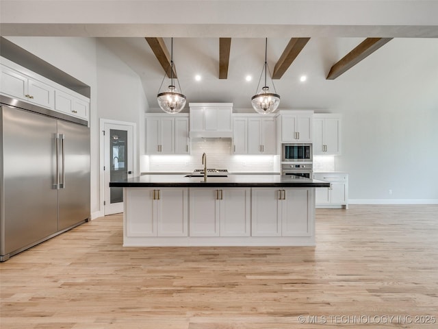 kitchen featuring an island with sink, built in appliances, white cabinets, and decorative light fixtures