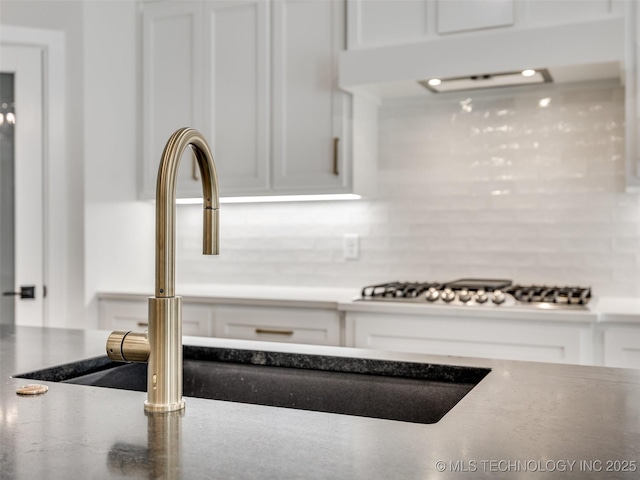 interior details with stainless steel gas cooktop, sink, decorative backsplash, and white cabinets