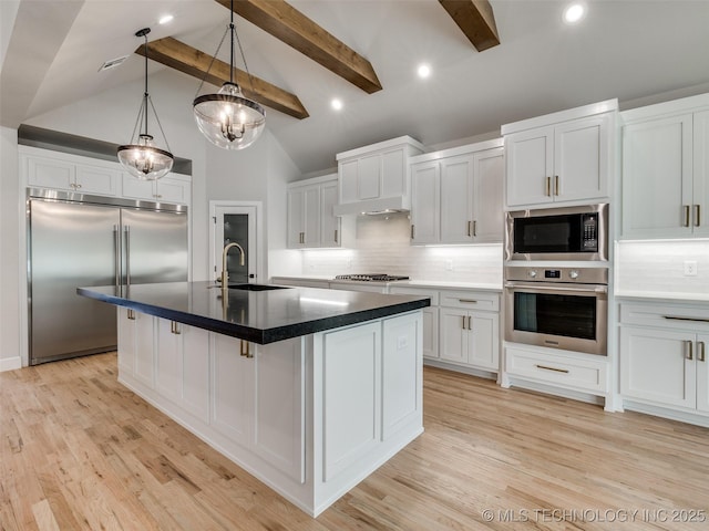 kitchen with white cabinetry, sink, decorative backsplash, a kitchen island with sink, and built in appliances