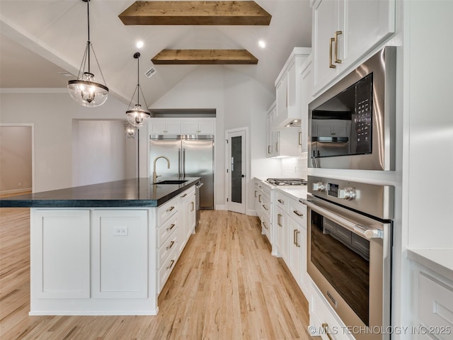 kitchen featuring built in appliances, an island with sink, and white cabinets