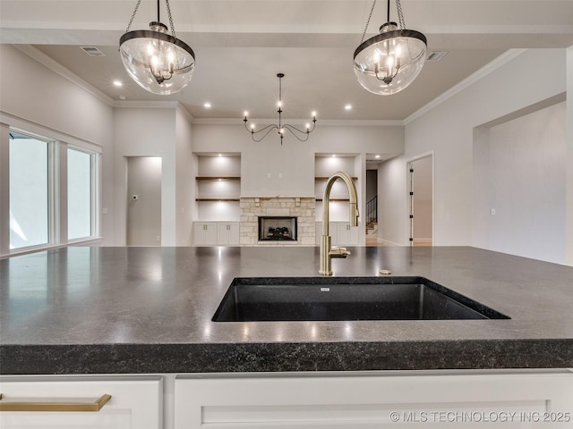 kitchen featuring pendant lighting, ornamental molding, a stone fireplace, and sink