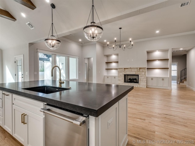 kitchen featuring decorative light fixtures, dishwasher, sink, white cabinets, and a center island with sink