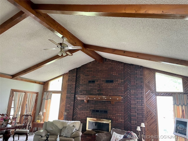 unfurnished living room with a textured ceiling, ceiling fan, a brick fireplace, and vaulted ceiling with beams