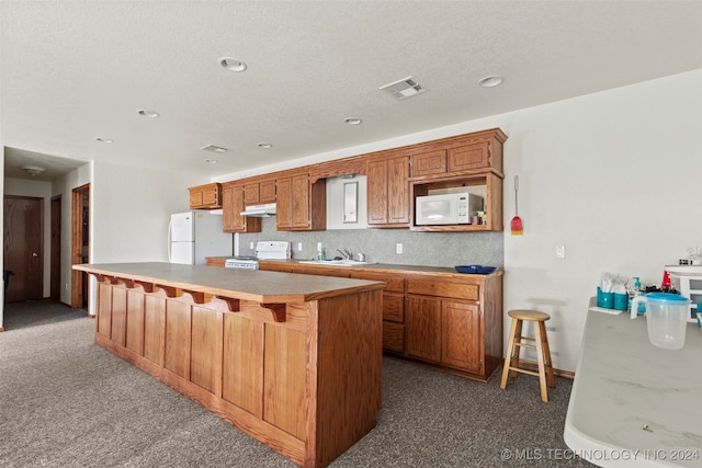 kitchen featuring white appliances, dark carpet, a kitchen island, sink, and a breakfast bar area