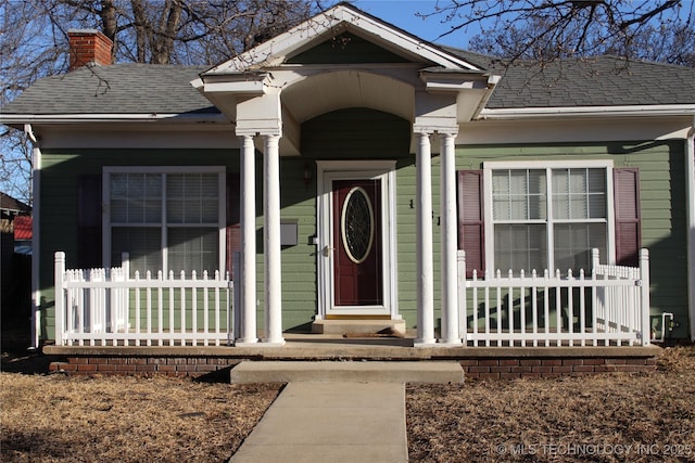 view of exterior entry with a shingled roof and a chimney