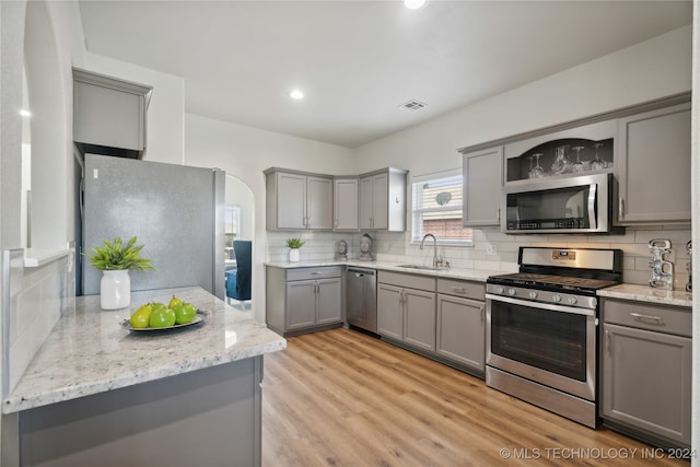 kitchen with tasteful backsplash, gray cabinets, appliances with stainless steel finishes, and light hardwood / wood-style floors