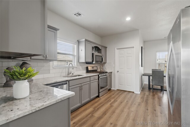 kitchen featuring backsplash, appliances with stainless steel finishes, sink, light stone counters, and light wood-type flooring