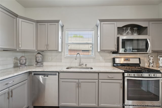 kitchen with gray cabinetry, light stone countertops, stainless steel appliances, and sink