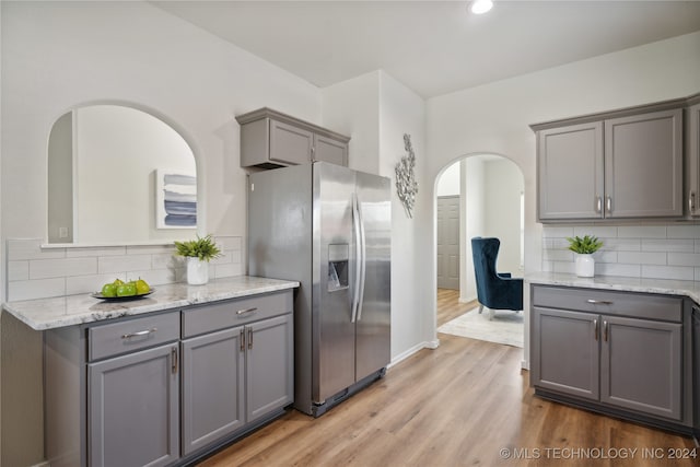 kitchen with backsplash, gray cabinets, light wood-type flooring, and stainless steel fridge with ice dispenser