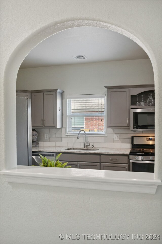 kitchen with gray cabinetry, backsplash, stainless steel appliances, and sink