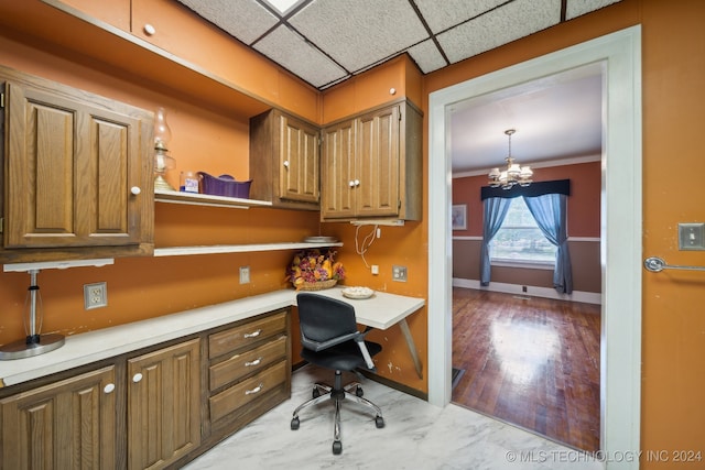 home office featuring built in desk, light hardwood / wood-style floors, a paneled ceiling, an inviting chandelier, and crown molding