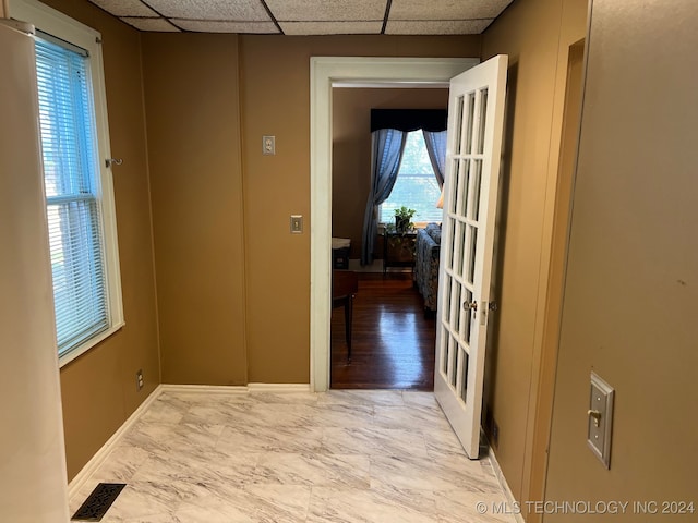 hallway featuring light hardwood / wood-style floors, a healthy amount of sunlight, and a paneled ceiling