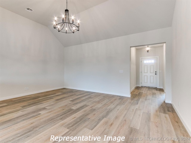 spare room with lofted ceiling, light wood-type flooring, and a chandelier