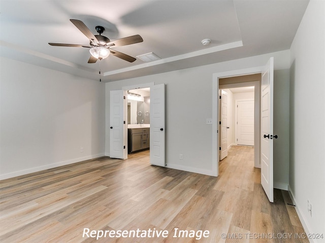 unfurnished bedroom with ceiling fan, ensuite bath, a tray ceiling, and light hardwood / wood-style floors