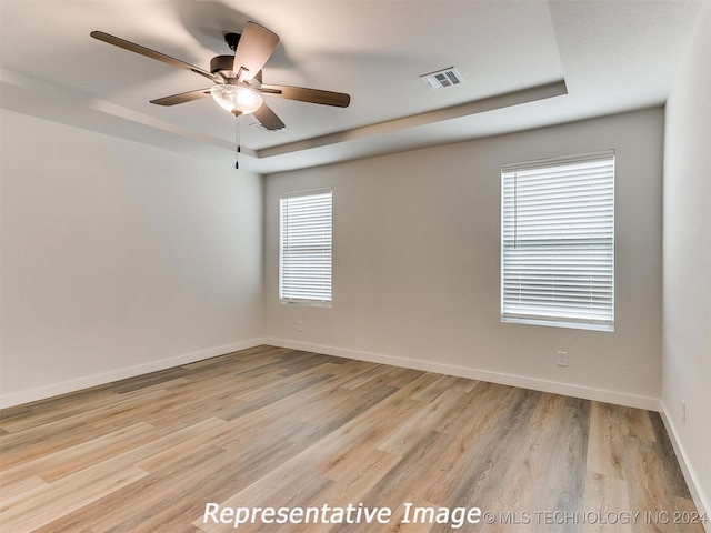 spare room featuring a tray ceiling, ceiling fan, and light hardwood / wood-style floors