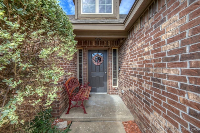 view of exterior entry with brick siding and roof with shingles