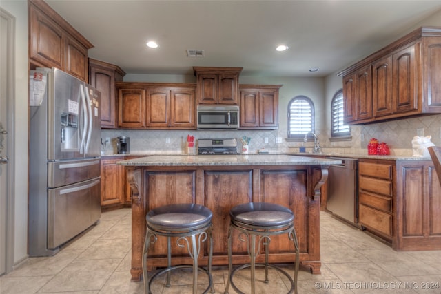 kitchen with appliances with stainless steel finishes, a center island, a breakfast bar, decorative backsplash, and stone counters