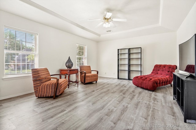 living area with a raised ceiling, ceiling fan, and hardwood / wood-style flooring