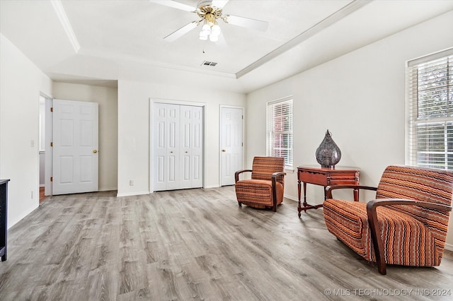 living area with light wood-type flooring, a tray ceiling, and ceiling fan