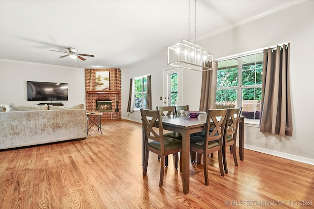 dining room featuring crown molding, light hardwood / wood-style flooring, ceiling fan with notable chandelier, and a brick fireplace