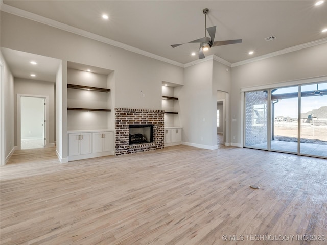 unfurnished living room featuring built in shelves, crown molding, a brick fireplace, ceiling fan, and light hardwood / wood-style floors