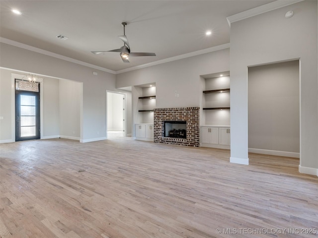 unfurnished living room with crown molding, built in features, light hardwood / wood-style floors, a brick fireplace, and ceiling fan with notable chandelier