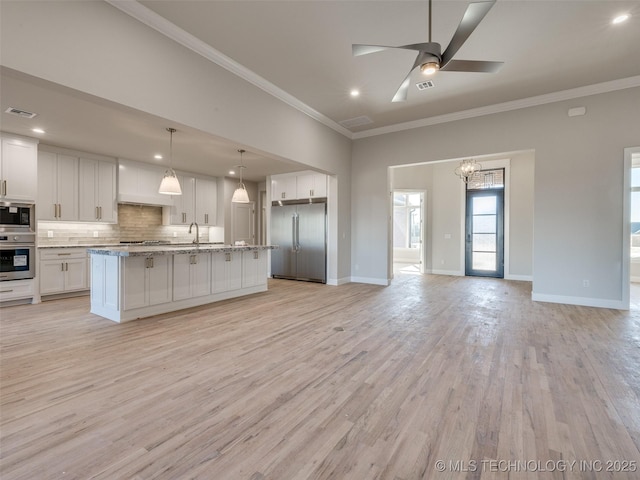 kitchen featuring crown molding, built in appliances, white cabinets, a center island with sink, and decorative light fixtures