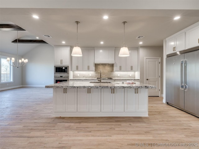 kitchen featuring sink, white cabinets, light stone counters, stainless steel appliances, and a center island with sink