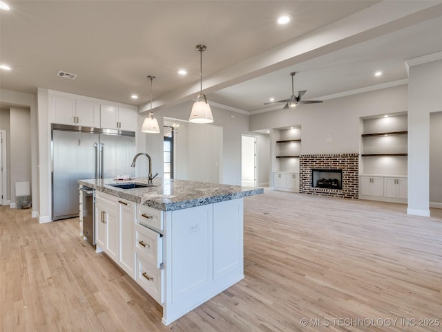 kitchen featuring pendant lighting, sink, white cabinetry, a kitchen island with sink, and light stone counters