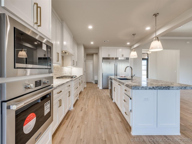 kitchen featuring sink, white cabinetry, hanging light fixtures, a kitchen island with sink, and light stone counters