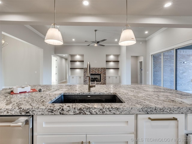 kitchen featuring sink, crown molding, stainless steel dishwasher, a fireplace, and white cabinets