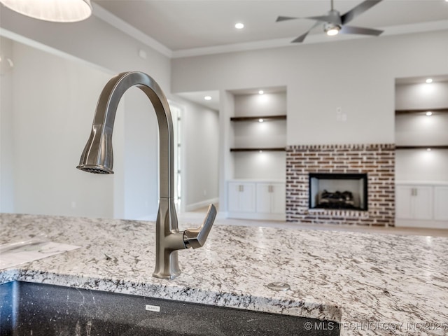 kitchen featuring sink, crown molding, ceiling fan, a fireplace, and light stone countertops