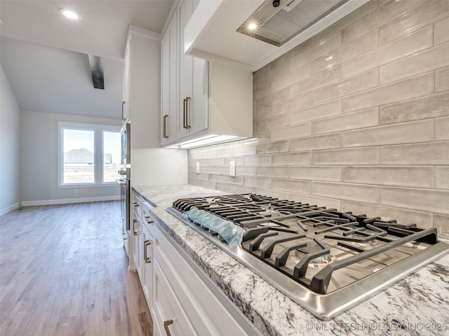 kitchen with appliances with stainless steel finishes, light stone counters, light hardwood / wood-style floors, white cabinets, and decorative backsplash