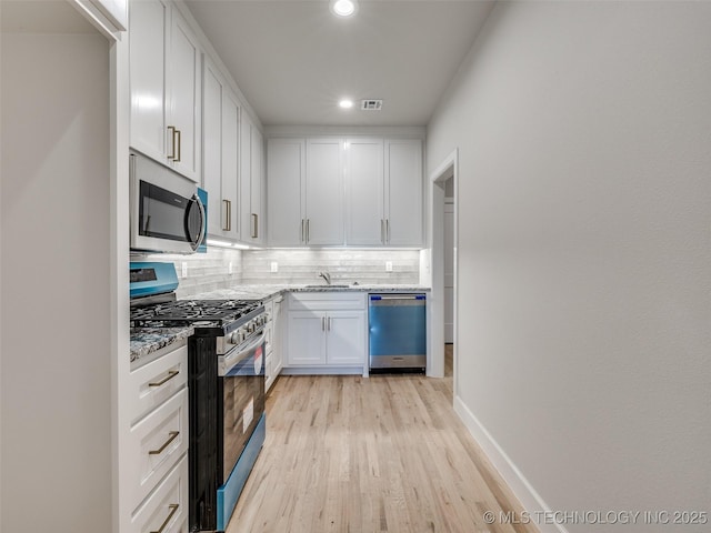 kitchen featuring white cabinetry, light hardwood / wood-style flooring, appliances with stainless steel finishes, light stone countertops, and decorative backsplash