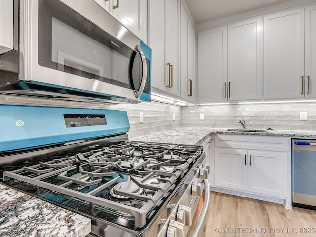 kitchen featuring appliances with stainless steel finishes, light wood-type flooring, white cabinets, and light stone counters