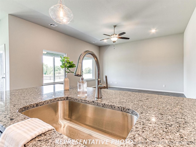 kitchen featuring light stone counters, ceiling fan, and sink