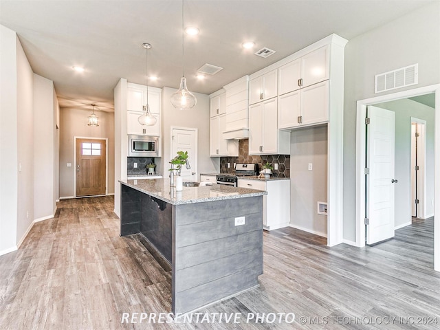 kitchen with light stone counters, stainless steel appliances, a kitchen island with sink, and light hardwood / wood-style flooring