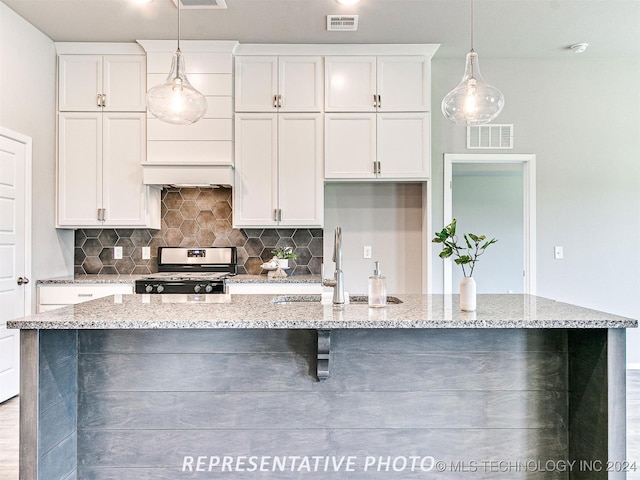 kitchen with a kitchen island with sink, white cabinetry, light stone counters, and stainless steel stove